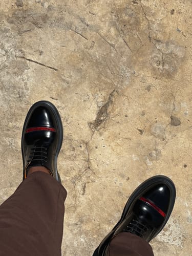 Customer's feet in black Lufiano Lace Up shoes with copper detail on a textured concrete surface