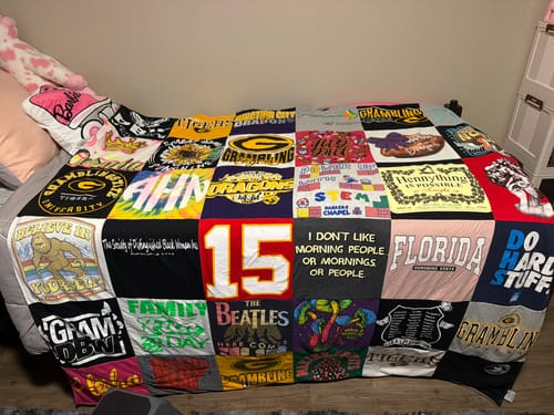 Customer's Project Repat T-Shirt Quilt laid out on a bed, featuring a colorful patchwork of various graphic shirts.