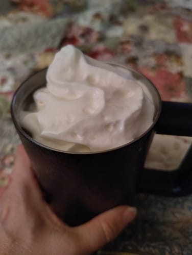 Customer's black Thicc Buddy mug held in hand, filled to the brim with whipped cream.