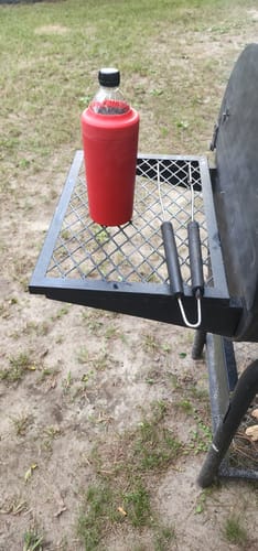 Customer's red Frost Buddy holding a drink bottle on a metal outdoor grill grate.