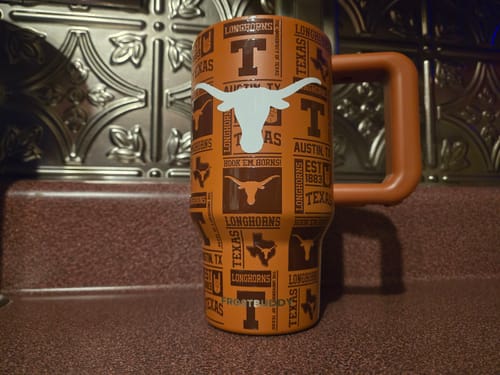 Customer's orange Thicc Buddy Texas Longhorns mug with logo pattern and handle, placed on a counter.
