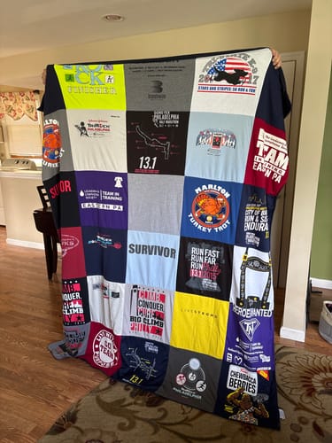 Customer's Project Repat T-Shirt Quilt held up, displaying a colorful patchwork of various race and event t-shirt logos.