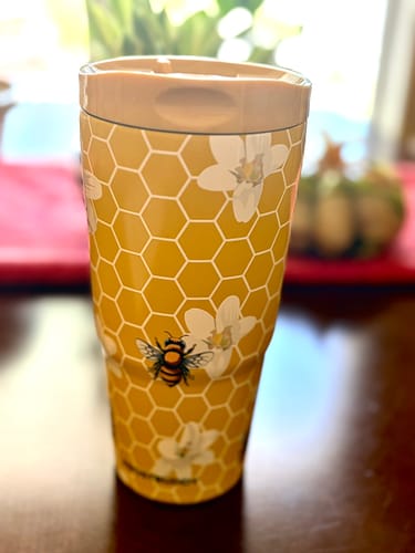 Customer's To-Go Buddy tumbler, yellow with a honeycomb and floral pattern, standing on a dark surface.