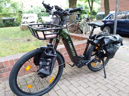 Customer's Lankeleisi MG600 Lite e-bike parked on a sidewalk with a front basket and attached storage bags.
