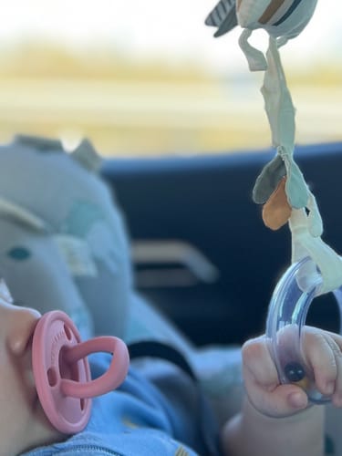 Customer's pink Nenina & Co. classic baby pacifier being used by a baby in a car.