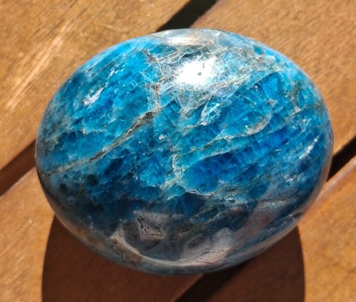 Customer's polished blue apatite stone showing natural textures, resting on a wooden surface.
