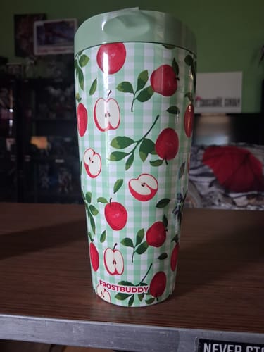 Customer's To-Go Buddy cup featuring a green gingham pattern with red apple illustrations, sitting on a table.