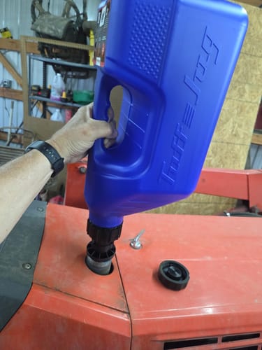 Reviewer's blue Tuff Jug being used to fill a red tractor's fuel tank.