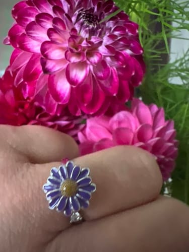Kliento žiedas „Calmy“ ant piršto, šalia ryškiai rožinių jurginų žiedų.
