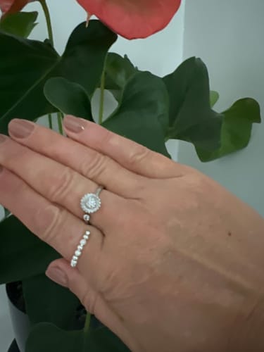 Reviewer's Calmy papuošalų rinkinio žiedai su blizgiais akmenėliais ant rankos prie augalo.