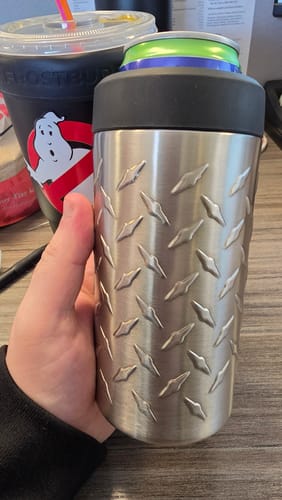 Customer's silver Diamond Plate Universal Buddy held in a hand next to a ghost-themed cup on a desk.