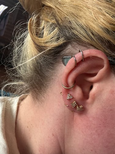 Reviewer wearing three gold Comfort Earrings on their ear lobe.