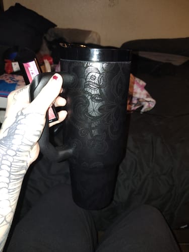 Customer's black Thicc Buddy 40oz tumbler with a lace pattern held in a tattooed hand.