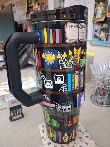 Customer's Thicc Buddy mug featuring a whimsical Halloween library design with books, skulls, and a potions book.