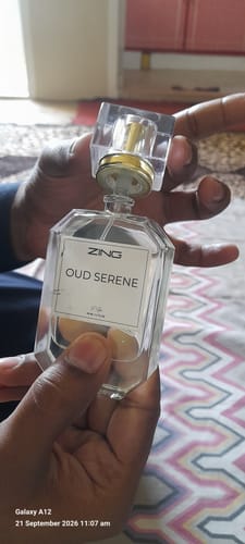 Customer's hand holding a clear, rectangular bottle of Zing Oud Serene perfume with a gold cap.