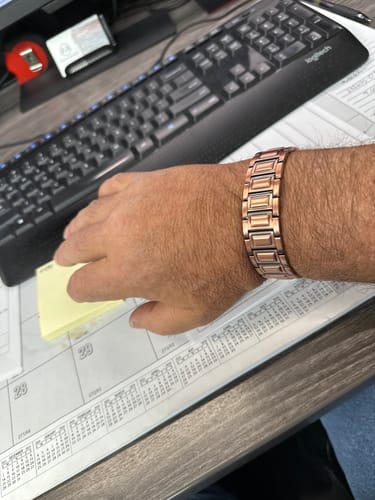 Customer's copper magnetic bracelet worn on their wrist while sitting at a desk with a keyboard.