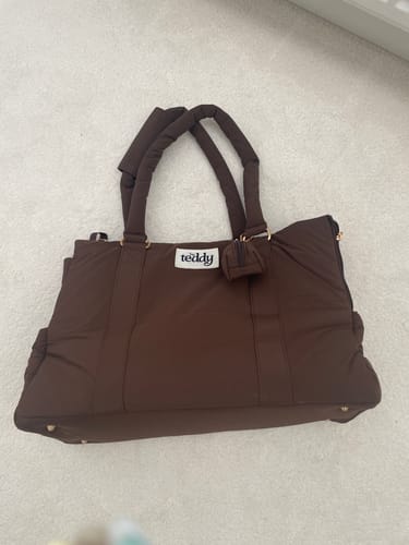 Customer's Chocolate Puffer Carrier showing the front canvas logo patch and attached mini bag on a carpeted floor.