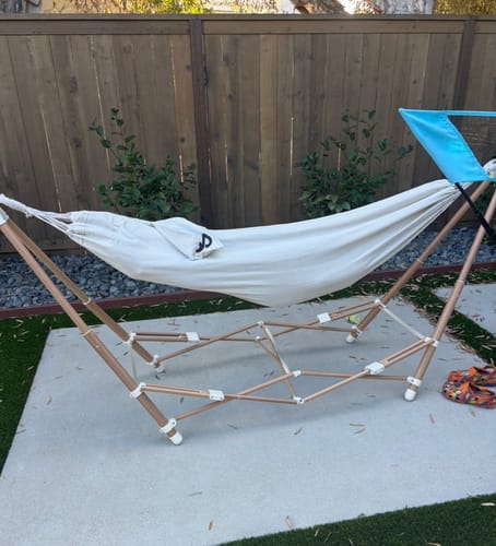 Customer's off-white Go Hammock with blue canopy, set up on a metal frame on a patio by a wooden fence.