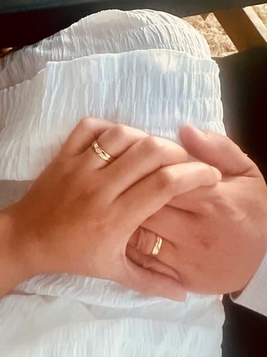 Customer's hands wearing The Curved Moissanite Couples Rings, with gold bands showing the unique curved design.