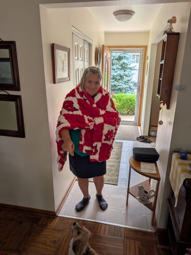 Reviewer standing in a doorway wearing a plush, red and white checkered University of Wisconsin Badgers blanket.