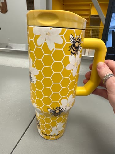 Customer's Thicc Buddy mug in yellow with bee and flower print being held in a hand