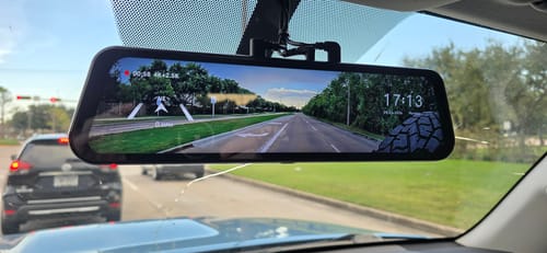 Reviewer's Wolfbox G900TriPro rearview mirror dash cam mounted on a vehicle windshield, displaying a road view.