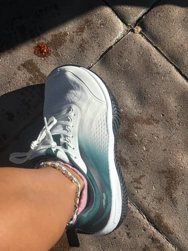 Customer's white and blue CUURT Muuv court shoe being worn, showing wide toe box while standing on a paved surface.