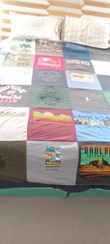 Customer's Project Repat T-Shirt Quilt spread out on a made bed, showcasing various colorful National Park graphics.