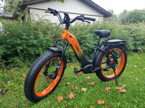 Customer's orange and black Lankeleisi MG600 Plus fat bike parked on a grassy lawn with green hedges in the background.