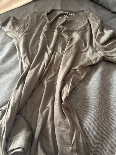 Kundenfoto des grauen Alpenwert Merino Langarmshirts, flach auf einer grauen Textiloberfläche ausgebreitet.
