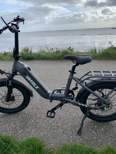 Customer's grey Vakole VT4 e-bike parked on an asphalt path with a water view in the background.