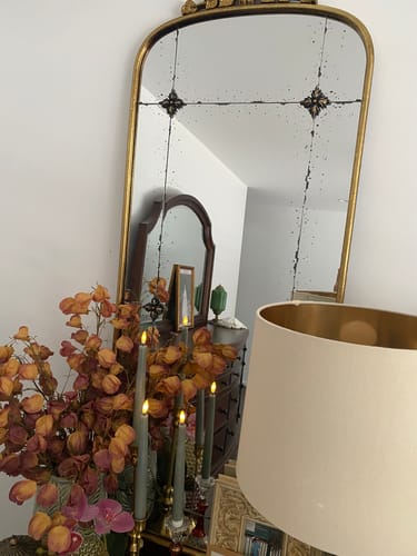 Customer's Thea French Provincial Arched Mirror in aged gold, shown in a cozy bedroom setting with flowers.
