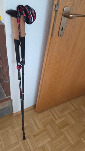 Kundenfoto der Rugova Pro 3 Wanderstöcke mit Korkgriffen und schwarzen Schlaufen, gelehnt an eine Holztür.