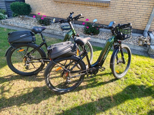 Customer's two dark green Lankeleisi MG600 Lite e-bikes parked on grass in front of a brick house.