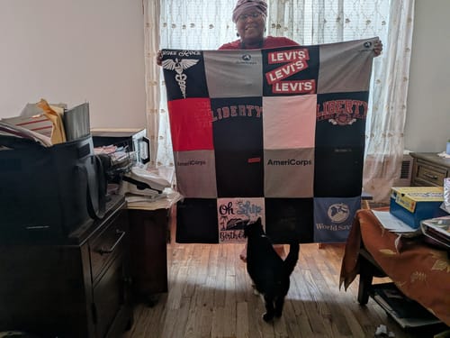 Customer's Project Repat T-Shirt Quilt held up by a person indoors with a black and white cat nearby.