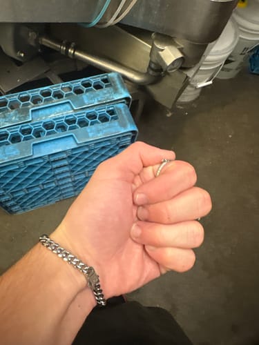 Customer's silver-tone Cuban Link Bracelet worn on a hand in a workshop setting with blue plastic crates in the background