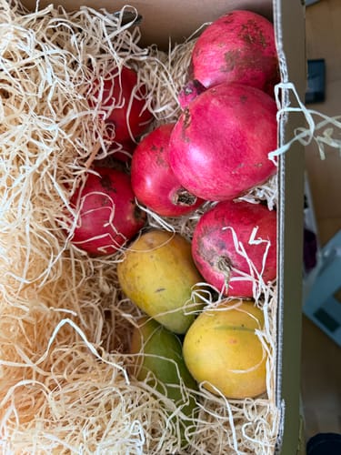 Customer's Mango & Granatapfel Bio Box showing red pomegranates and yellow mangoes nestled in straw packaging.