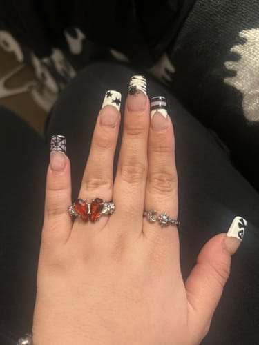 Customer's hand wearing two silver MINI RINGS featuring a butterfly design with red stones and a celestial motif.