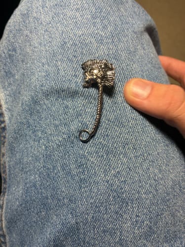 Customer's metallic Punk Safety Pin featuring a detailed skull with a mohawk, held against a denim background.