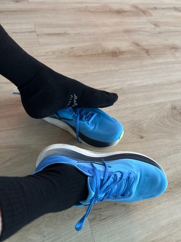 Kunden-Merino-Socken in Schwarz getragen in leuchtend blauen Laufschuhen auf einem Holzboden.