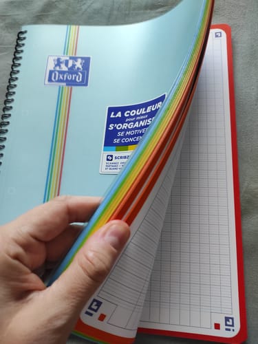 Reviewer's hand holding a blue Oxford Color System notebook, showing the vibrant multi-colored interior page borders.