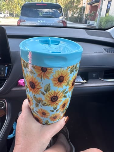 Customer's Sunflower Skies To-Go Buddy cup held in a car, showing the bright floral pattern and blue lid.