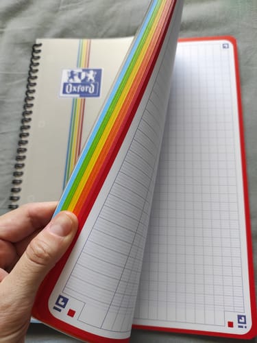 Reviewer's hand opening an Oxford COLOR SYSTEM spiral notebook to show the colorful grid paper edges.