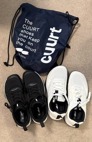 Customer's CUURT Muuv court shoes in black and white pairs, displayed next to a dark blue drawstring bag.