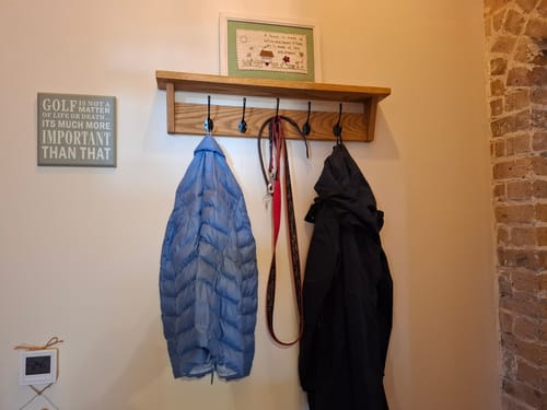 Customer's wall-mounted solid oak coat rack with a storage shelf and five hooks, holding coats and a dog lead.