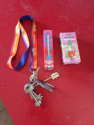 Customer's THC-A Pre-Roll Cali Blend packaging next to a branded lanyard and keys on a red surface.