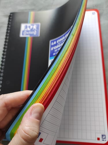 Customer's hand holding open an Oxford Color System spiral notebook, showing multicolored page edges.