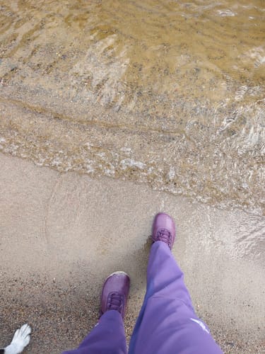 Customer's purple Vaistoa Uoma 2 -paljasjalkavaelluskengät walking on a sandy beach shore.