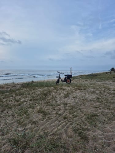 Customer's Vakole Y20 Pro e-bike parked on a sandy beach shore under a cloudy sky.