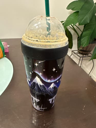 Customer's To-Go Buddy cup featuring a nightfall mountain print, filled with iced coffee on a dark table.